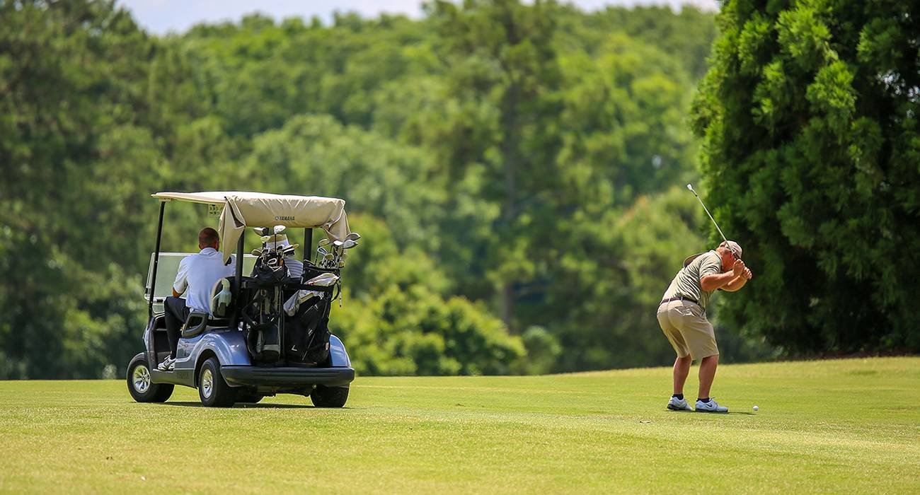 A man hits the ball while someone waits in the golf cart.